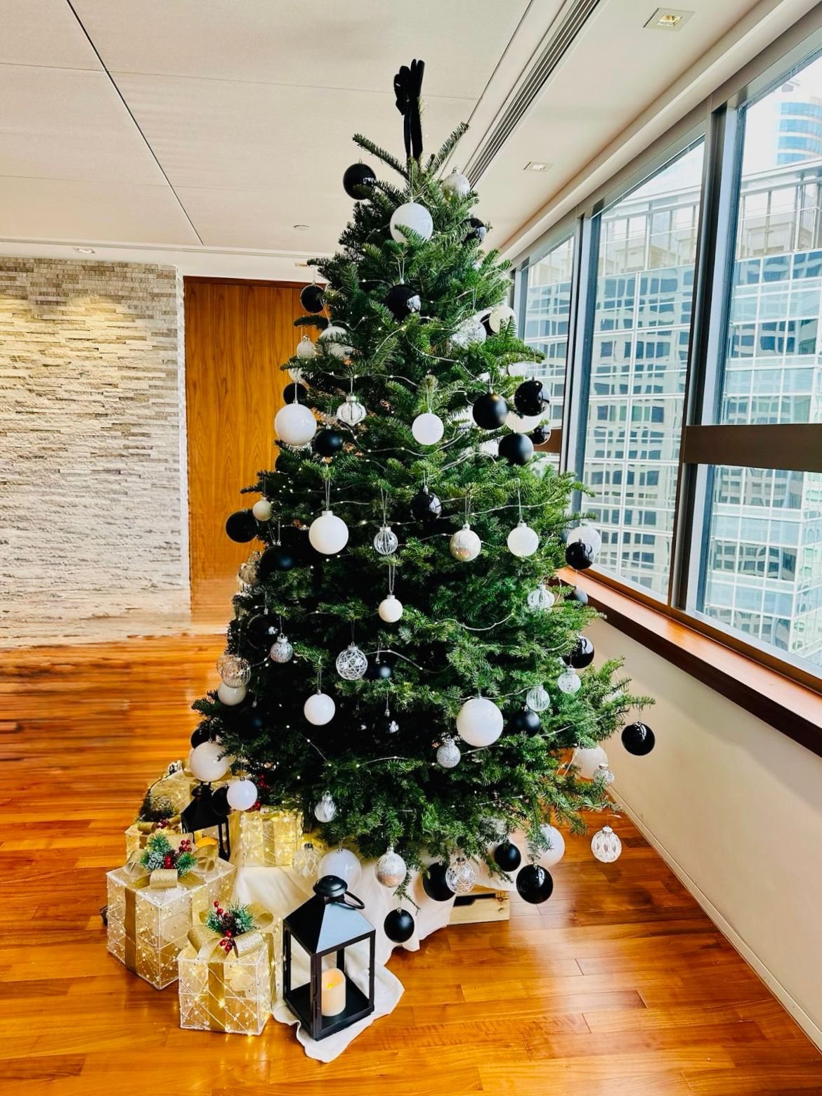 Christmas tree with black, white and silver ornaments beside office windows