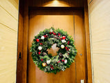 Fresh Christmas wreath with red berries, pine cones and ornaments on a wooden door